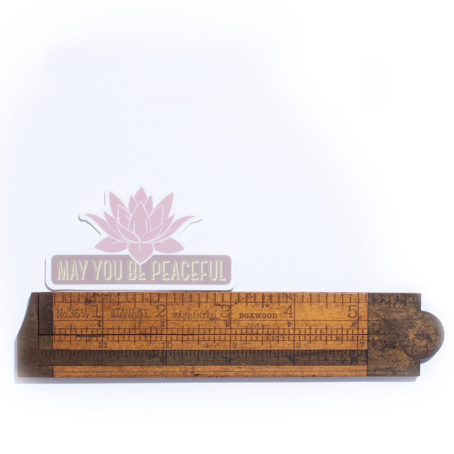 Wooden ruler with 'May you be peaceful' text and lotus flower on a white background.
