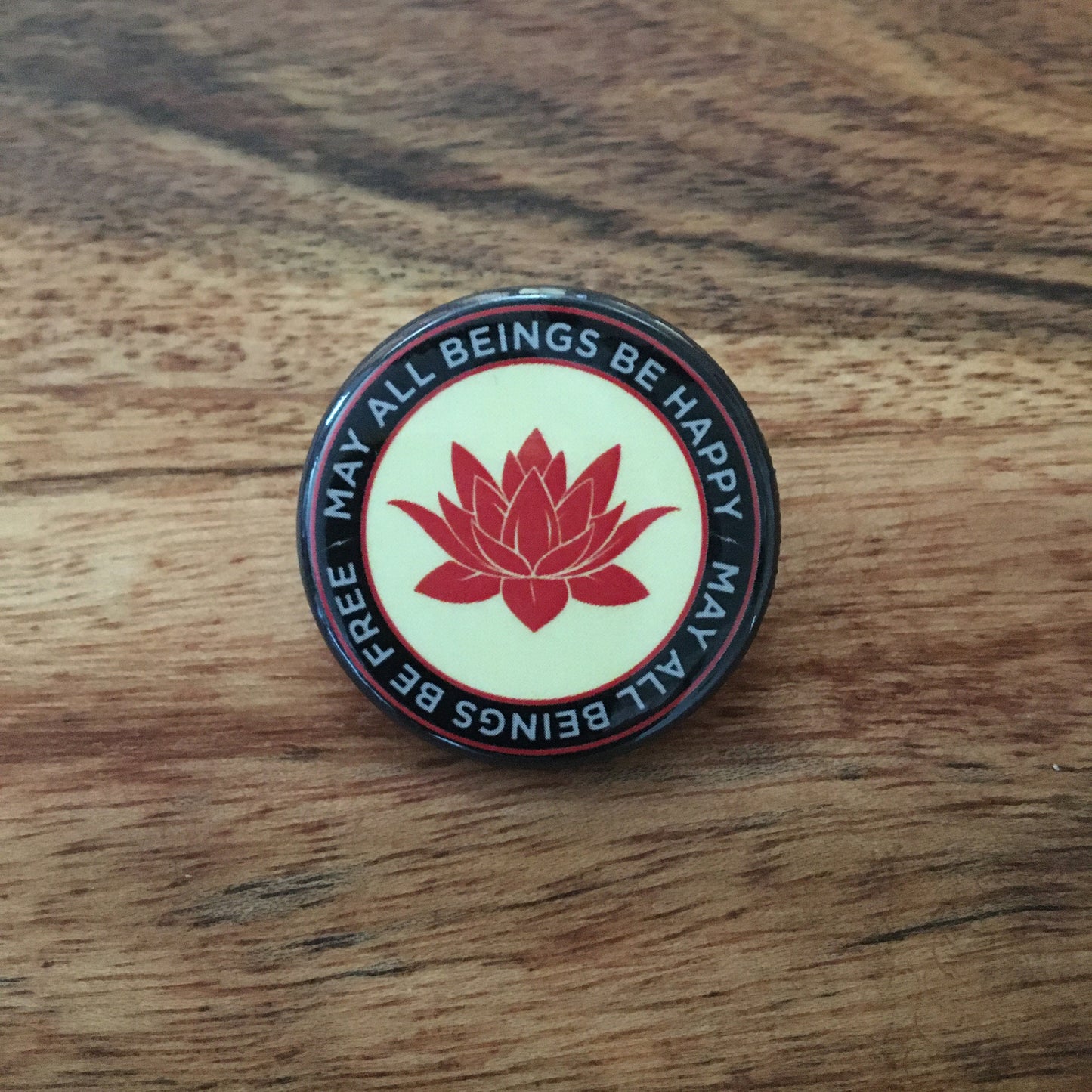 1.25" pin back button with a red lotus flower design and the text, may all beings be free may all beings be happy.