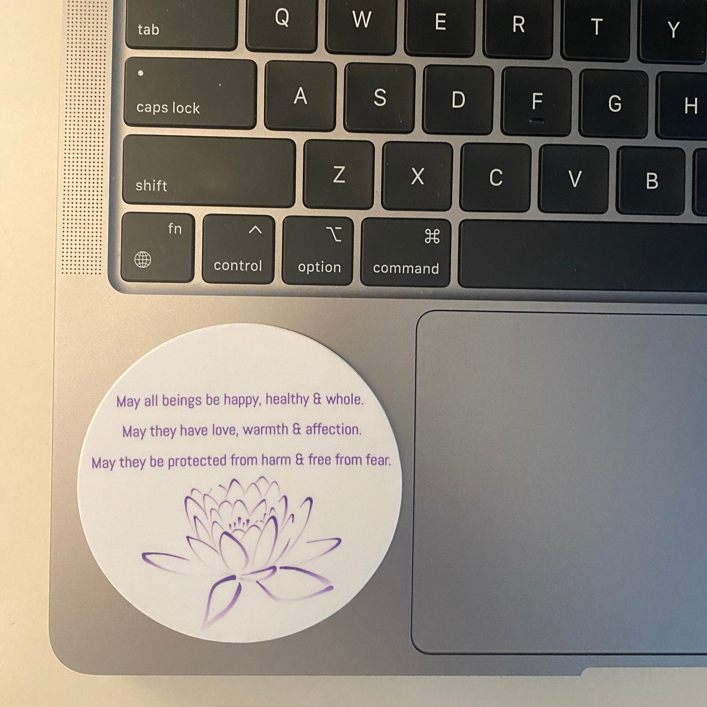 Laptop keyboard with a 3" circular sticker with Buddhist prayer and a lotus design.
