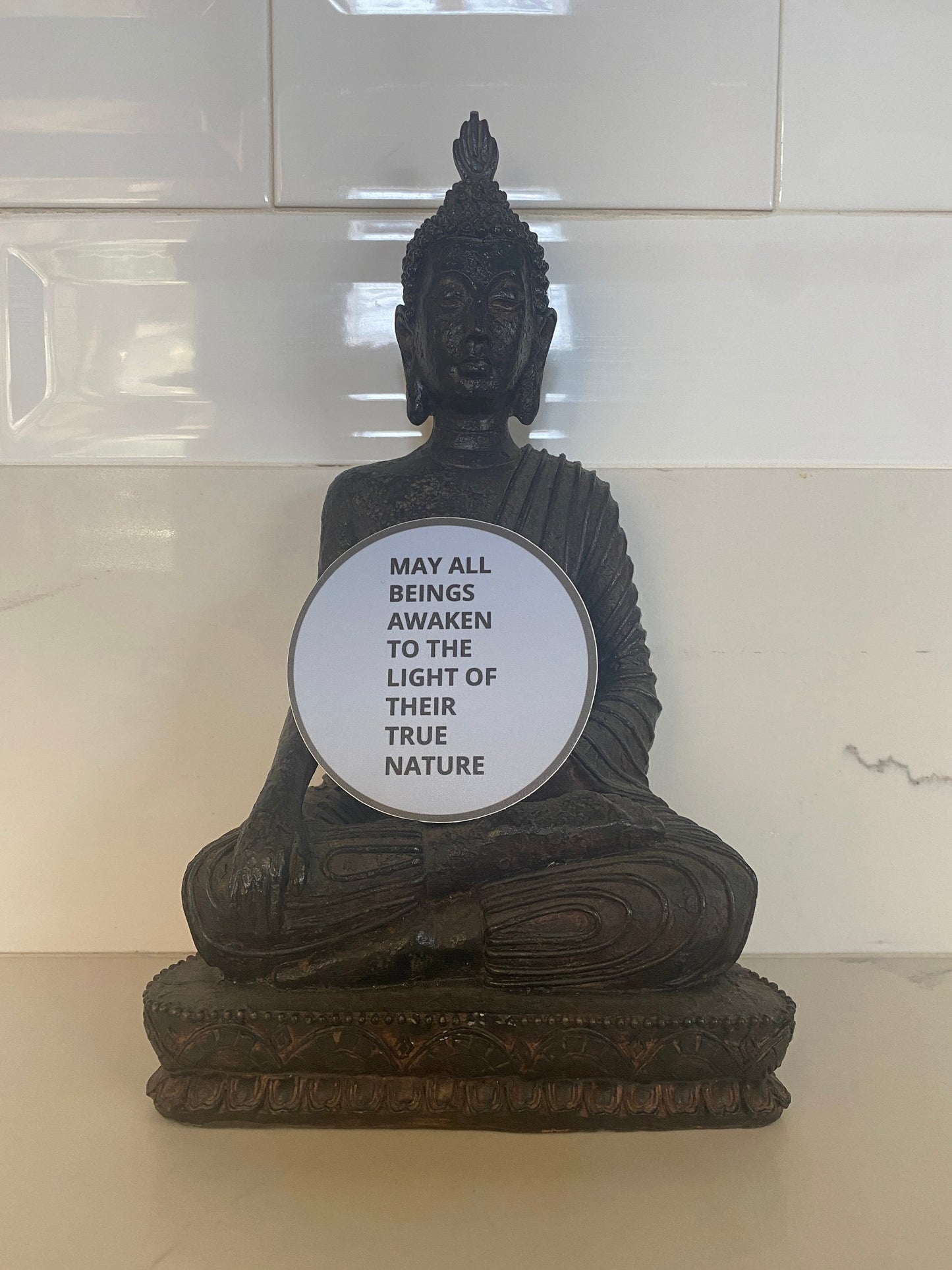 Buddha statue with a circular sticker with the text, may all beings awaken to the light of their true nature.