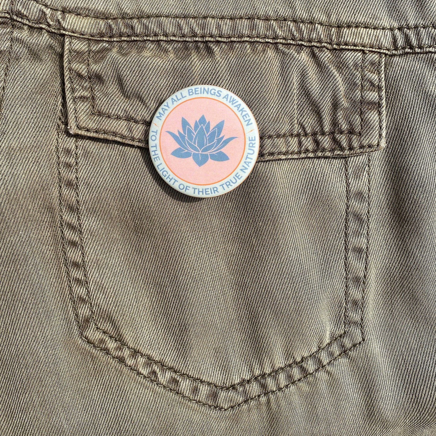 Pin with lotus flower design on a pocket of a beige jacket.