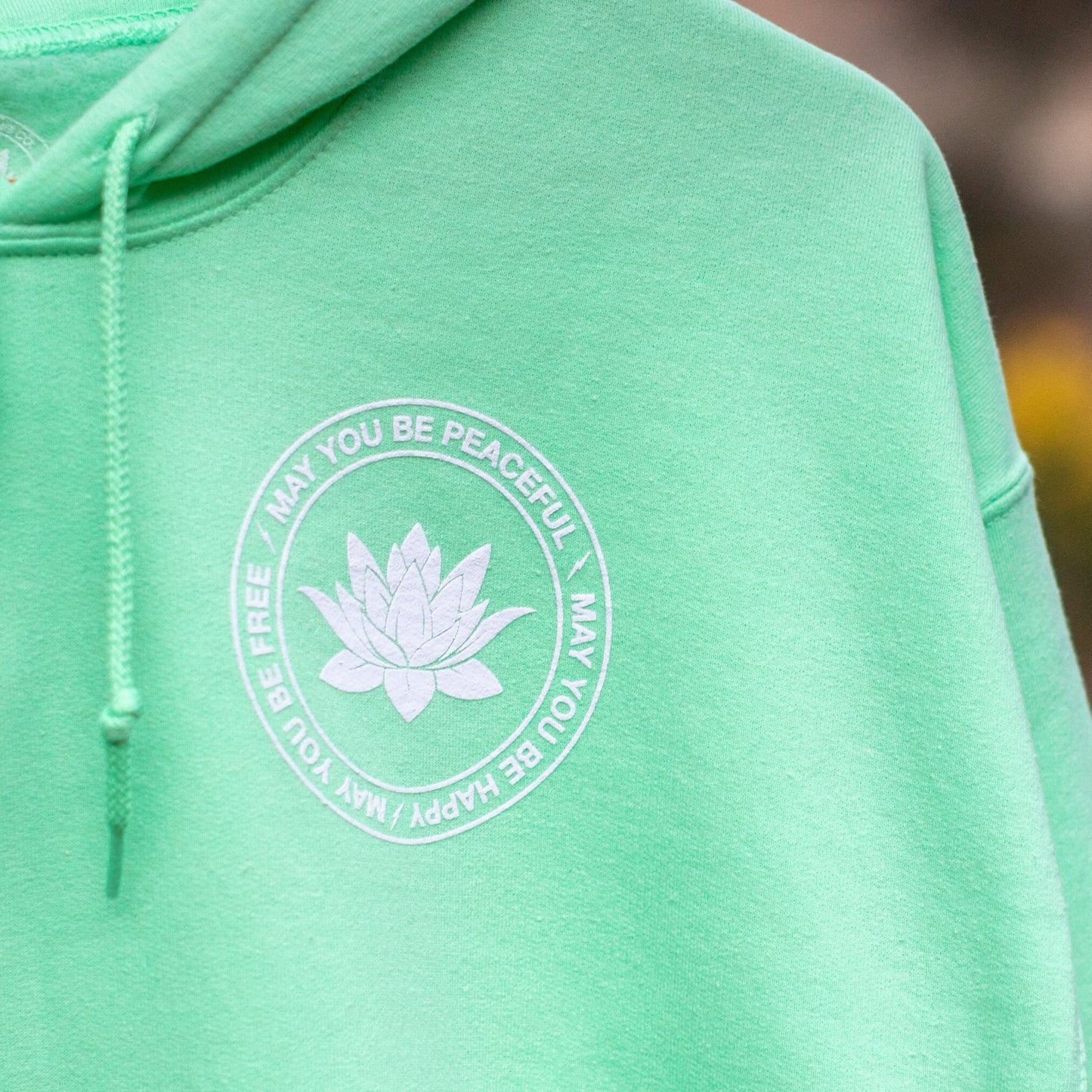 Green hoodie with a white lotus flower with the text may you be happy may you be peaceful may you be free.