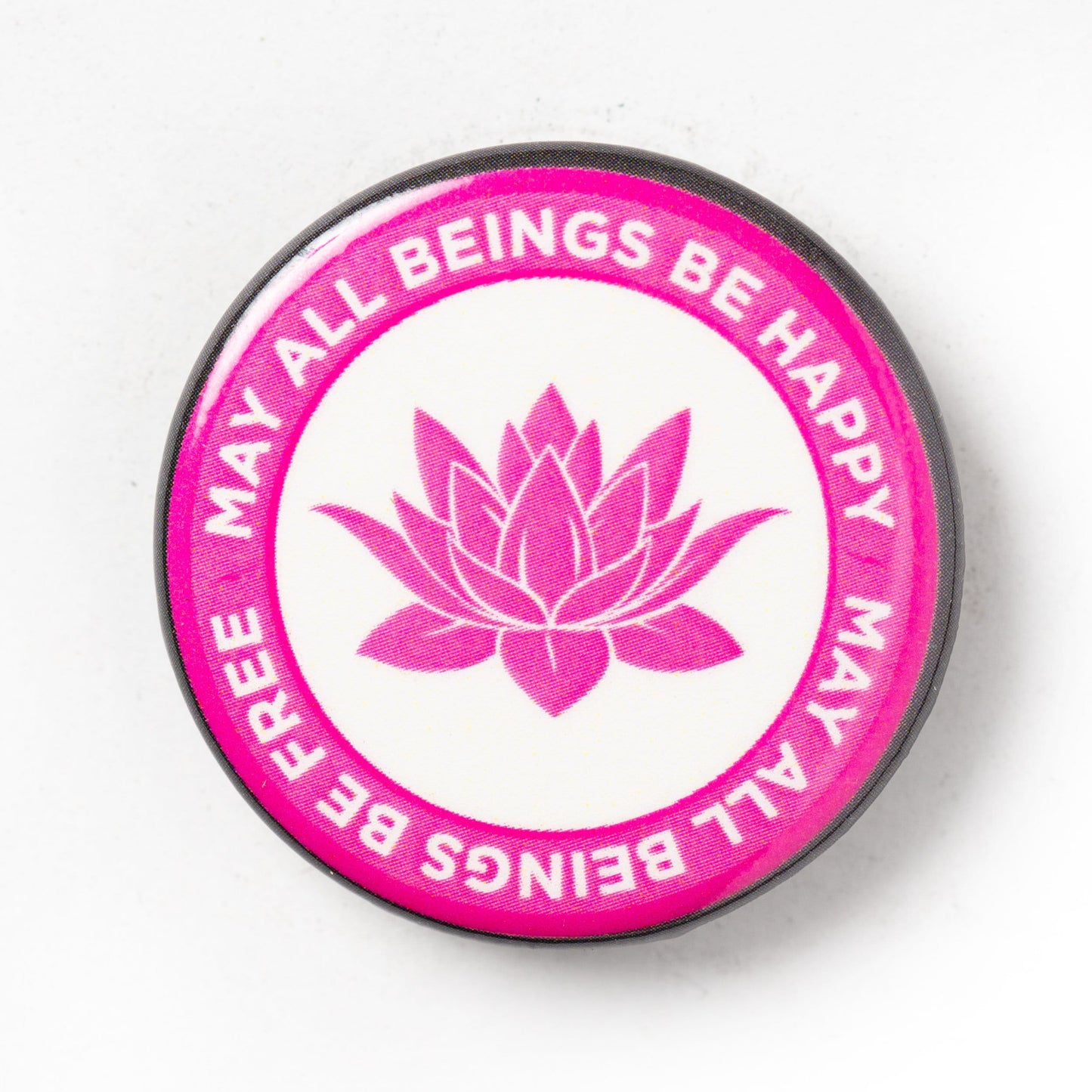 Circular pink and white button with lotus flower and text, may all beings be happy may all beings be free on a white background