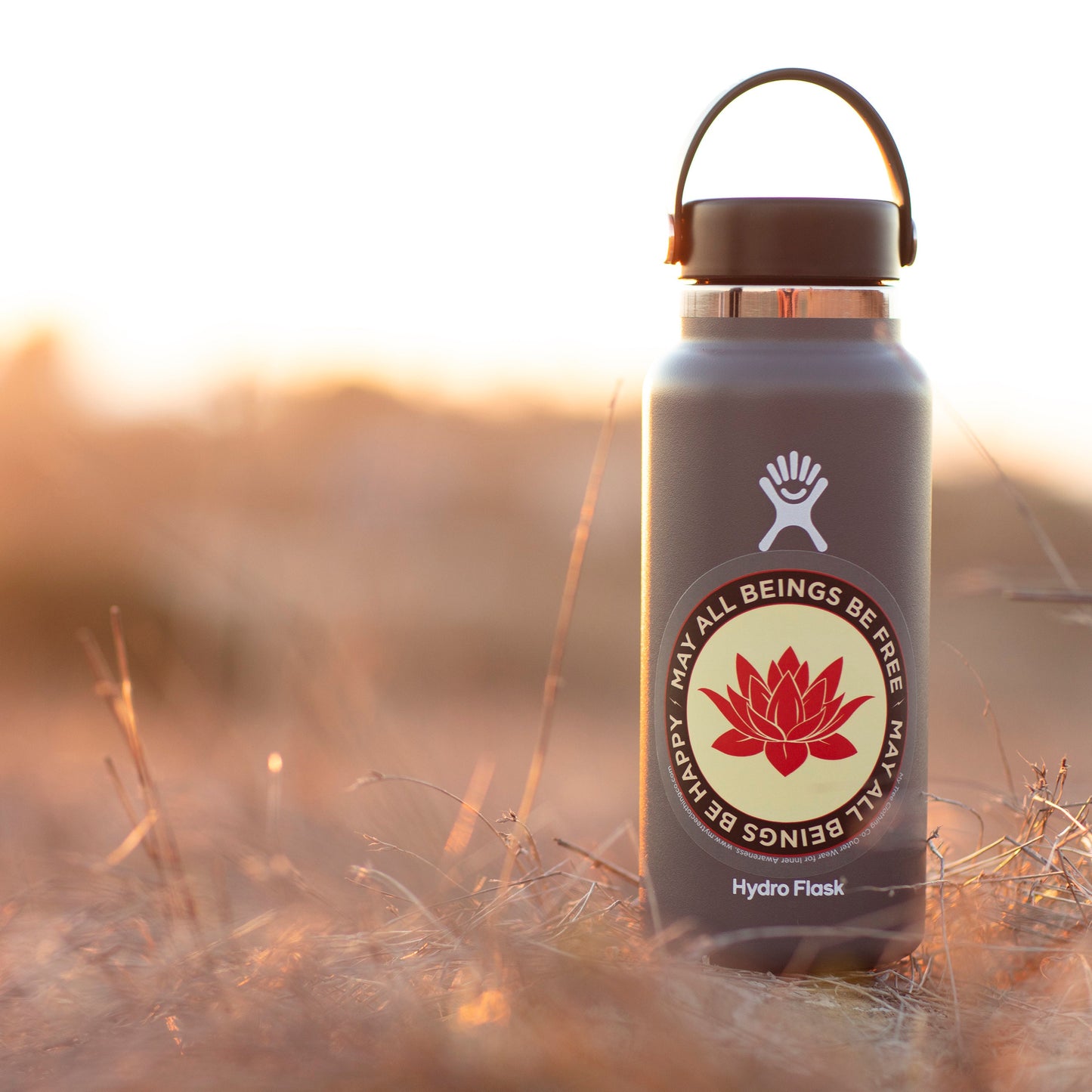 Hydro Flask bottle with a red lotus flower sticker with the text, may all beings be free may all beings be happy, in a natural setting