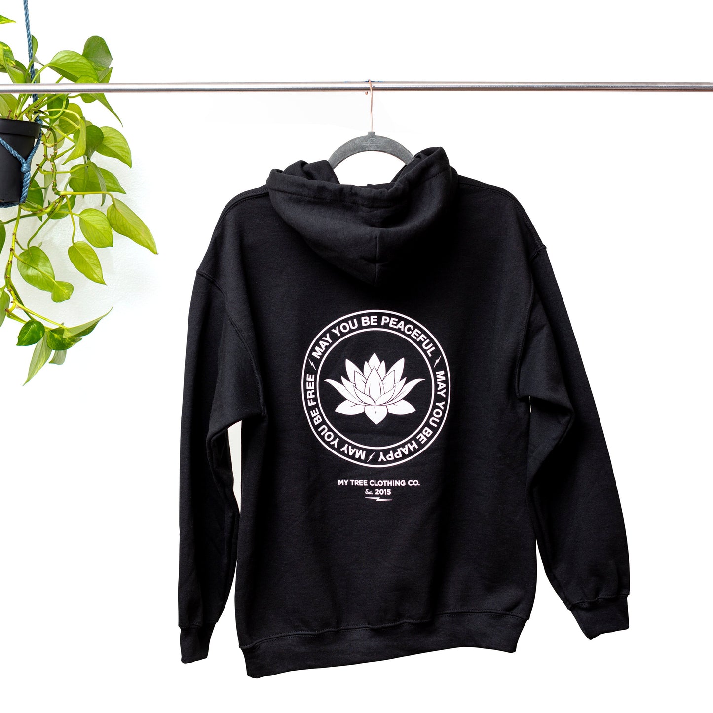 Backside view of black hoodie with a white lotus and the mettā prayer, 'may you be peaceful may you be happy may you be free.'