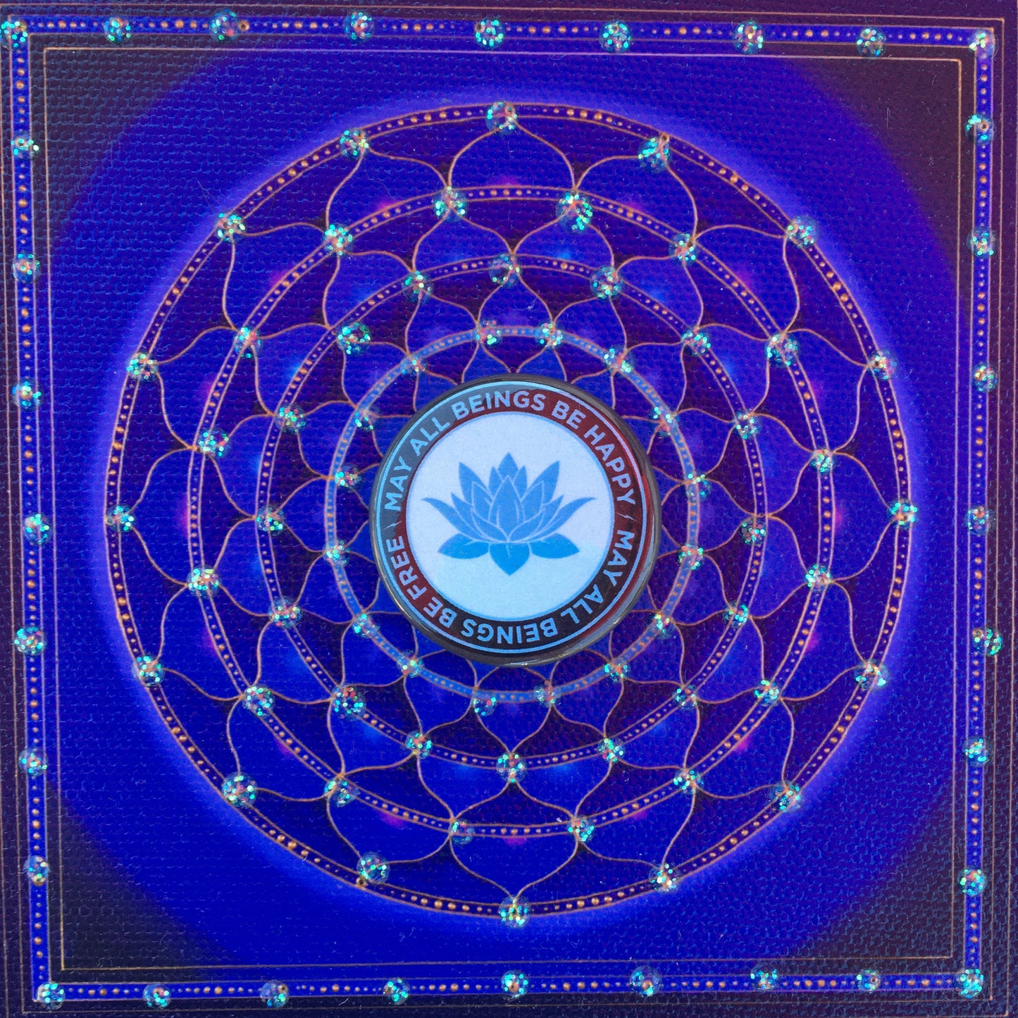 Decorative blue and black button with a lotus symbol and 'All Beings Be Happy May All Beings Be Free' text on a blue background.