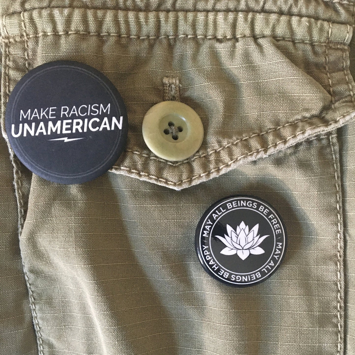 Two buttons on a beige jacket, one with 'Make Racism Unamerican' text and the other with a lotus flower design that reads, may all beings be free may all beings be happy.