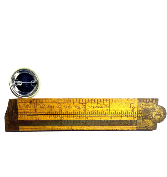 Wooden ruler with measurement markings and a round metal badge on a white background.