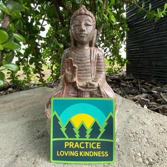 Buddha statue with a 3" square ultra thin magnet with trees and a sunrise and the text 'Practice Loving Kindness' in front of greenery.