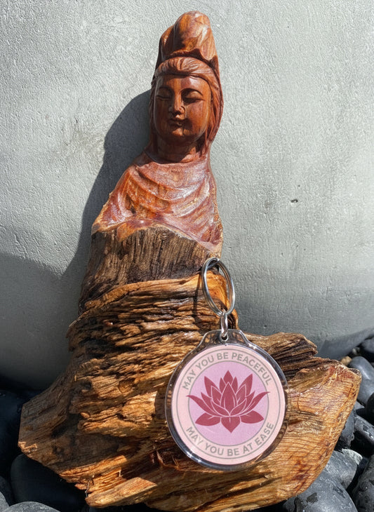 Wooden Bodhisattva seated figure with a 2" pink lotus keychain that reads, may you be peaceful may you be at ease on a stone surface.