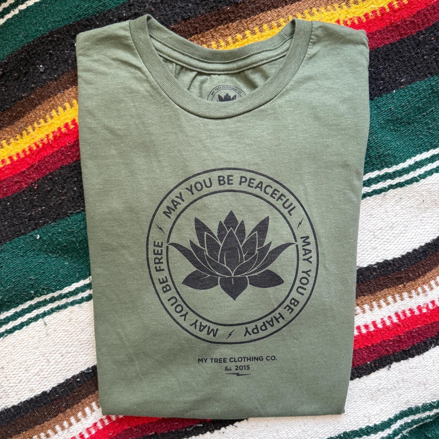 Folded green t-shirt with a black lotus flower design on a colorful striped background