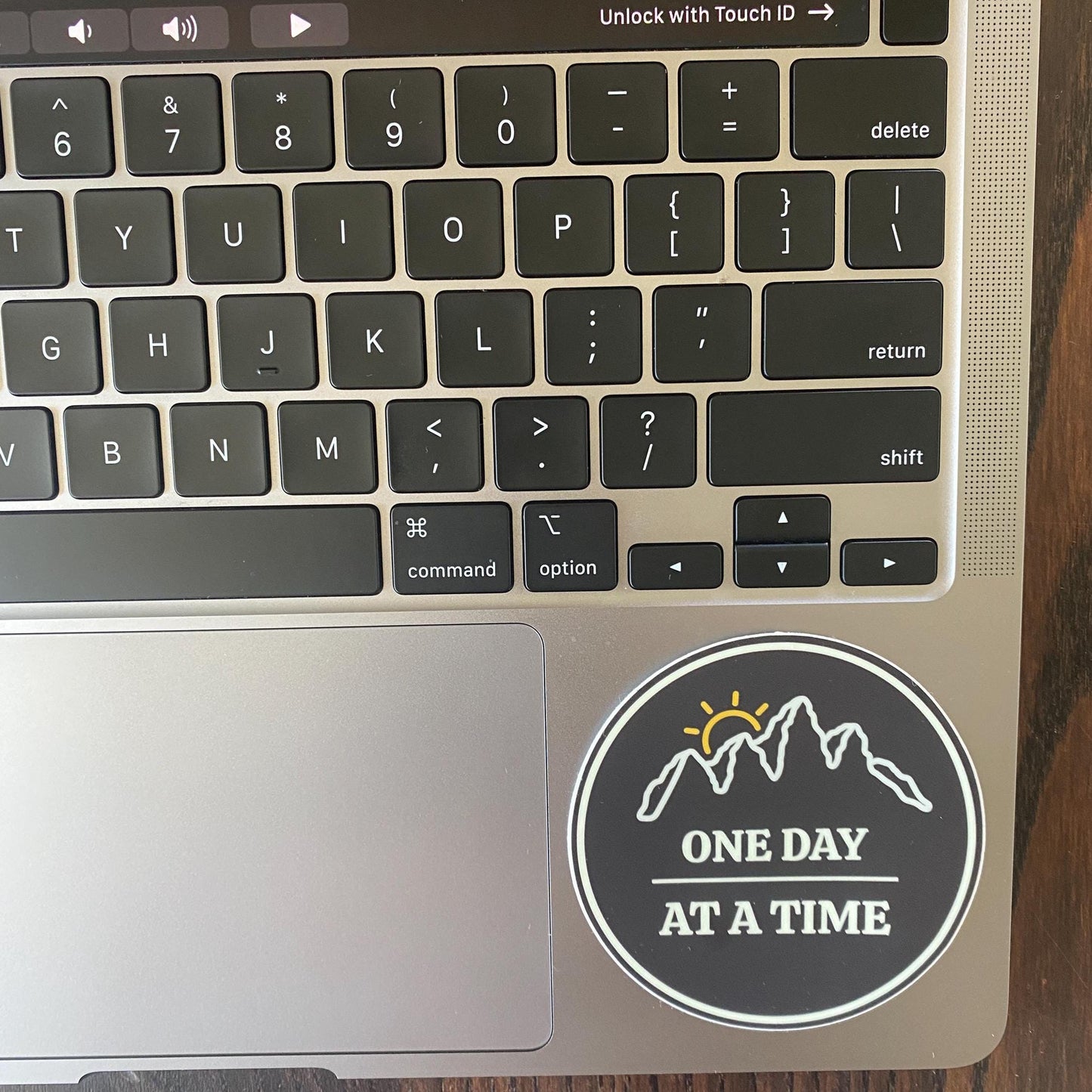 Laptop keyboard with a sticker reading 'One Day at a Time' on a wooden surface
