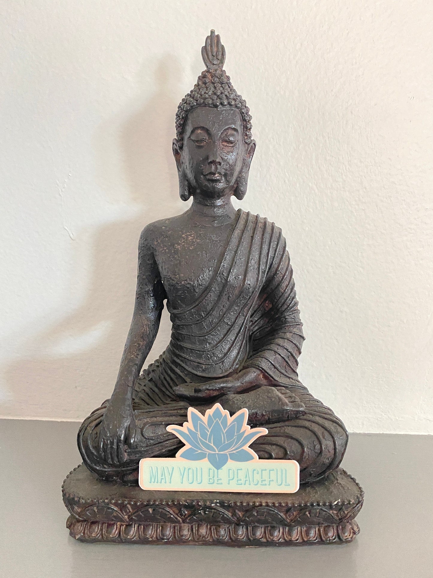 Buddha statue with a lotus flower sticker with 'May you be peaceful' text.