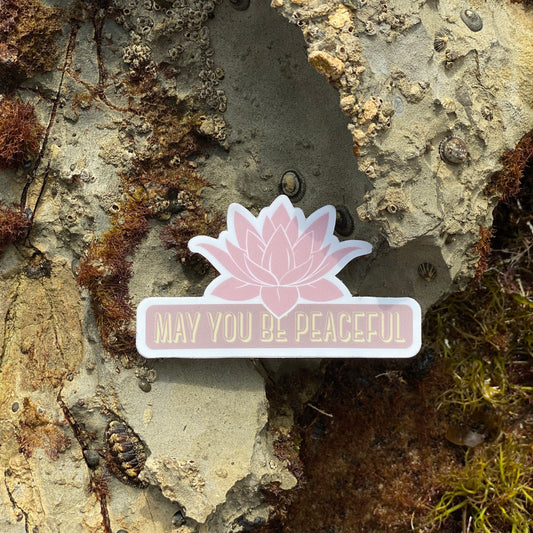 Pink lotus flower sticker with 'May you be peaceful' text on a textured stone background