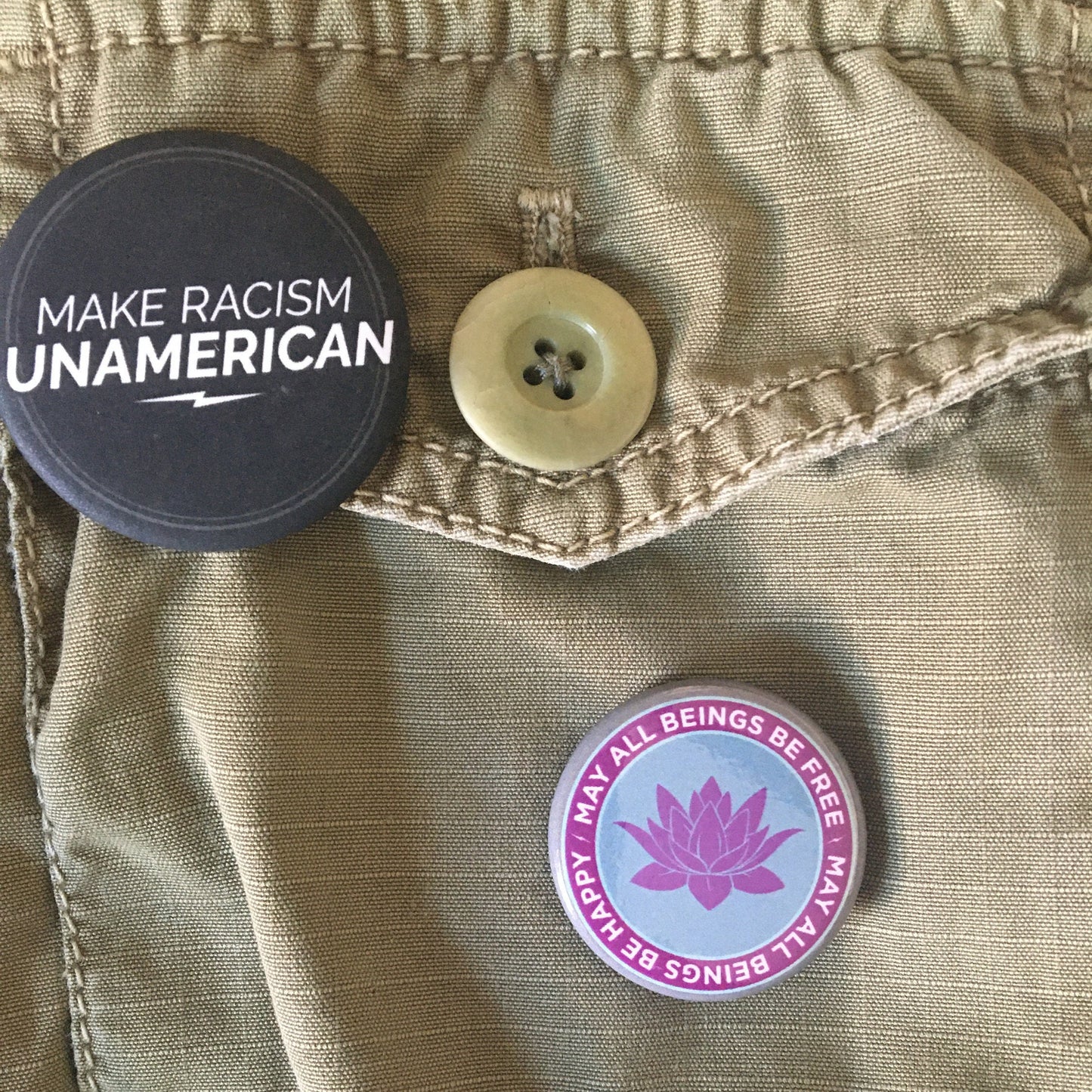 Button with 'Make Racism Unamerican' text on a jacket with another button featuring a 1.25" round pin back button with a purple lotus design and text, may all beings be free may all beings be happy.