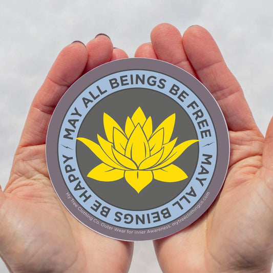 4" circular sticker with yellow lotus flower and text, 'may all beings be free may all beings be happy' held between two hands against a white background.