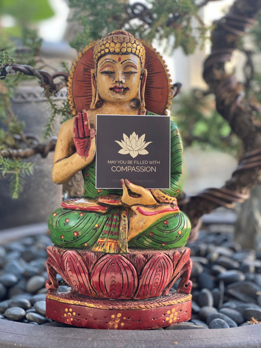 Buddha statue holding a 2" square lotus flower sticker with text 'May you be filled with compassion' in front of a Bonsai tree.
