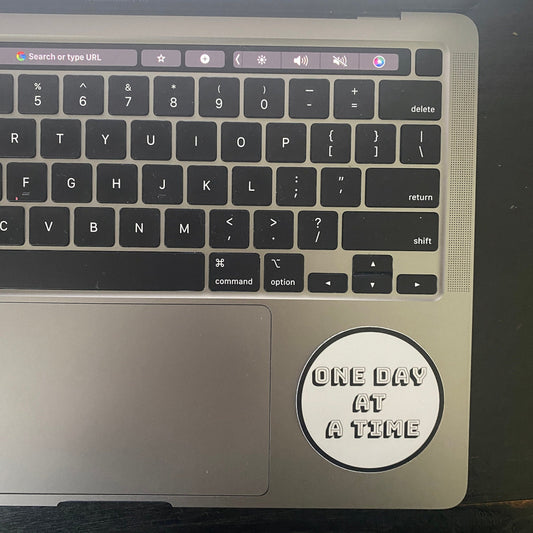 Laptop with a 12 Step recovery sticker 'One Day at a Time' on the palm rest area.