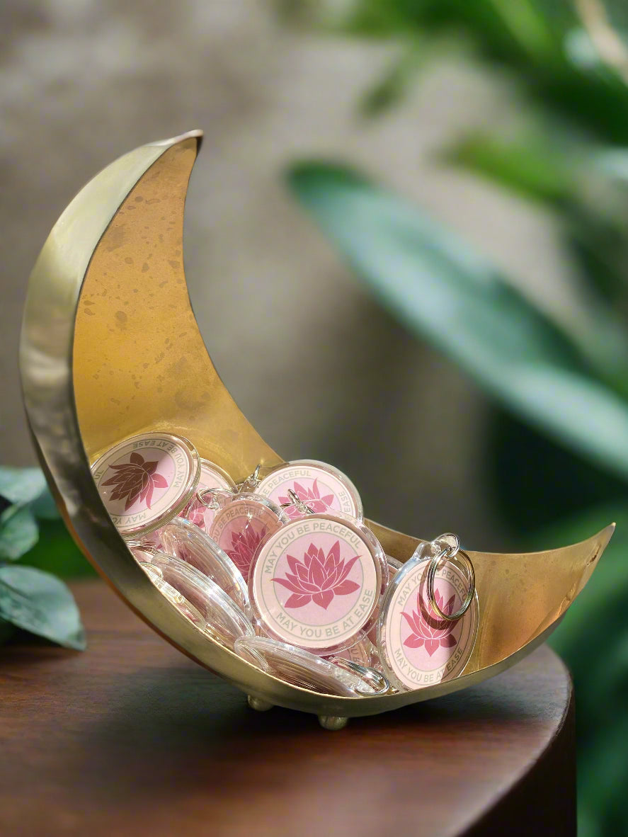 Gold crescent-shaped dish with a bunch of pink lotus keychains with the Buddhist message, may you be peaceful may you be at ease.
