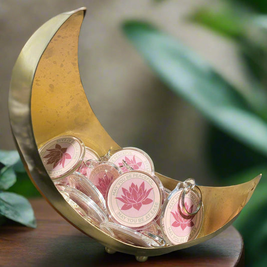 Gold crescent-shaped dish with a bunch of pink lotus keychains with the Buddhist message, may you be peaceful may you be at ease.