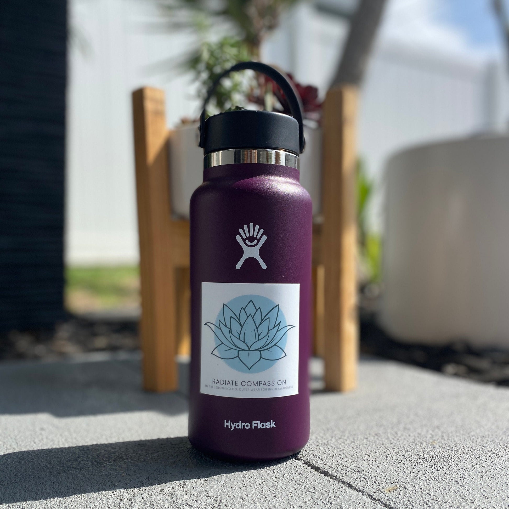 Purple Hydro Flask water bottle with a 3" square sticker with a blue lotus design and text, radiate compassion.