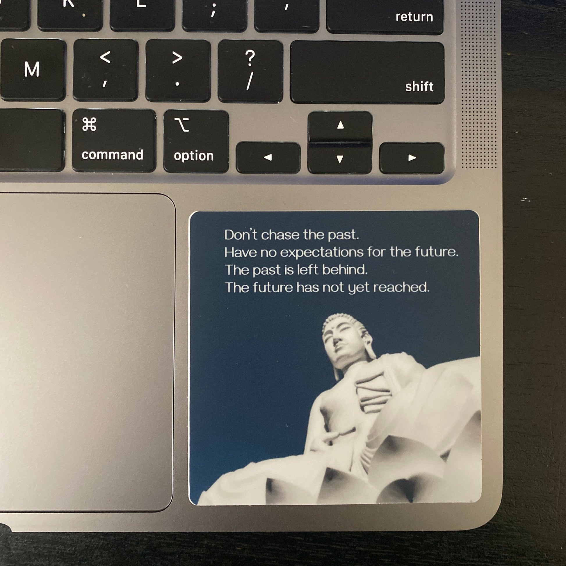 Laptop with a 3" round sticker with a Buddha statue and text, "don't chase the past, have no expectations for the future, the past is left behind, the future has not yet reached" on the palm rest area.