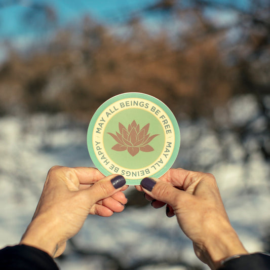 Two hands holding a 4" circle lotus flower design and text, MAY ALL BEINGS BE FREE MAY ALL BEINGS BE HAPPY.