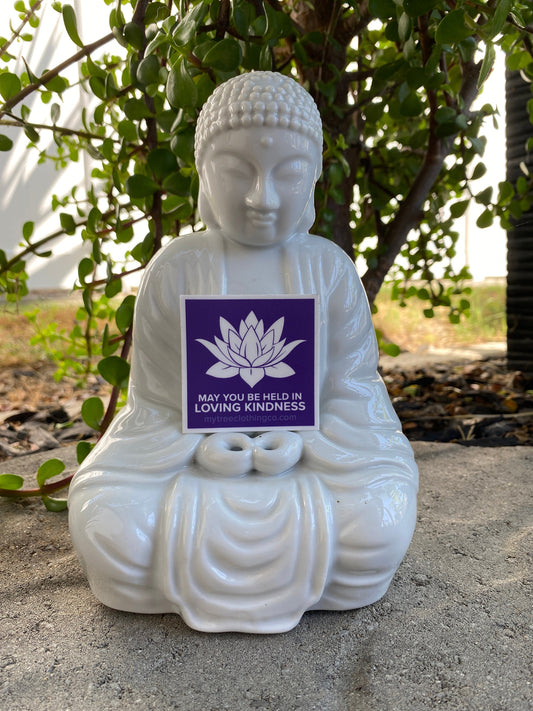 White Buddha statue with a 2" square purple and white  lotus sticker with the words, may you be held in loving kindness.