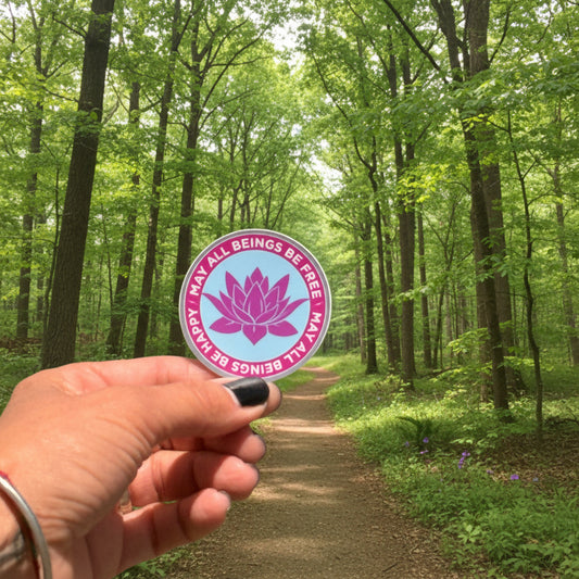 Hand holding a 2" round lavender lotus sticker with the words, may all beings be free-may all beings be happy.