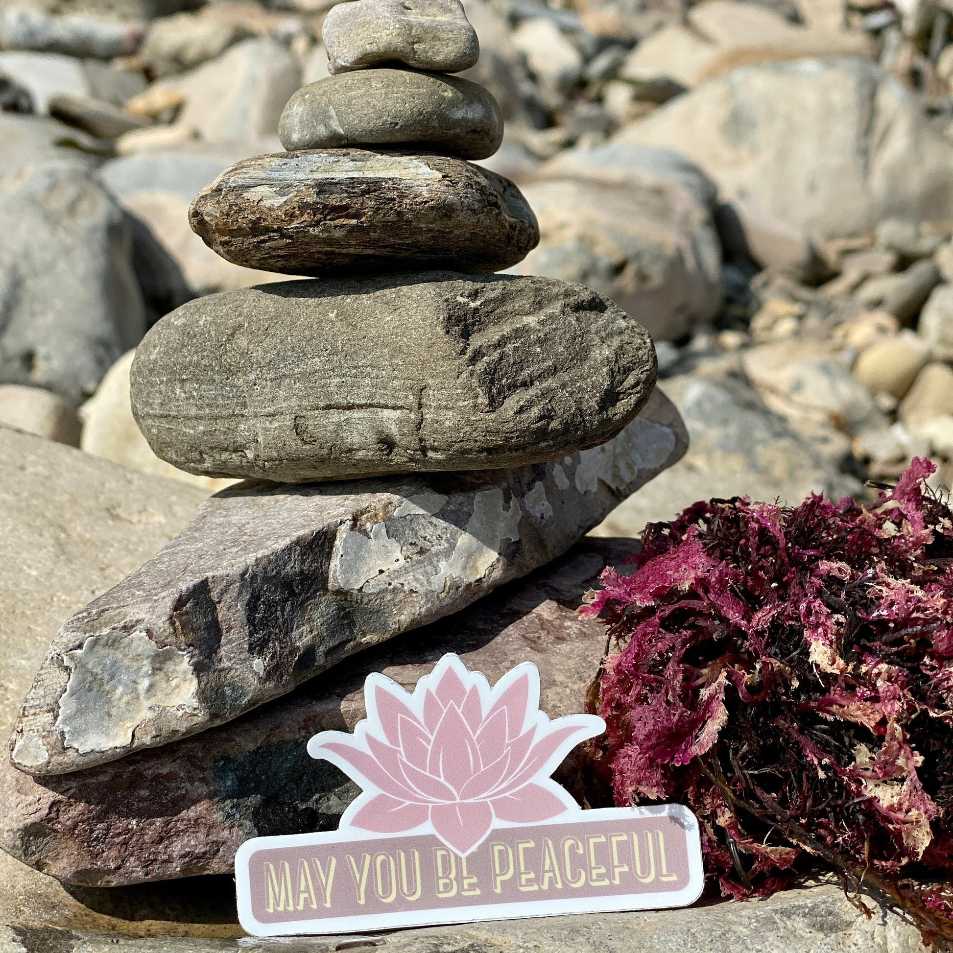Stack of stones with a pink lotus flower with the text, may you be peaceful.