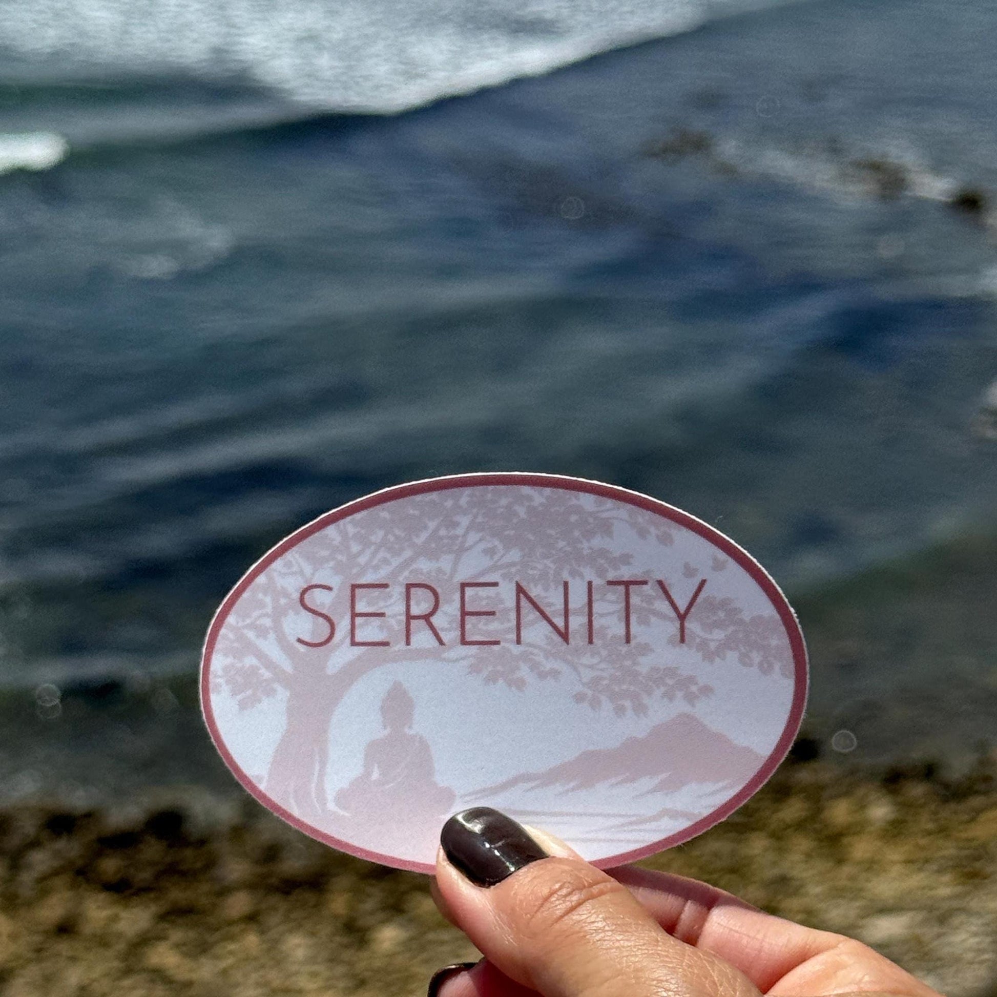 Sticker with 'Serenity' text held over a blurred natural background