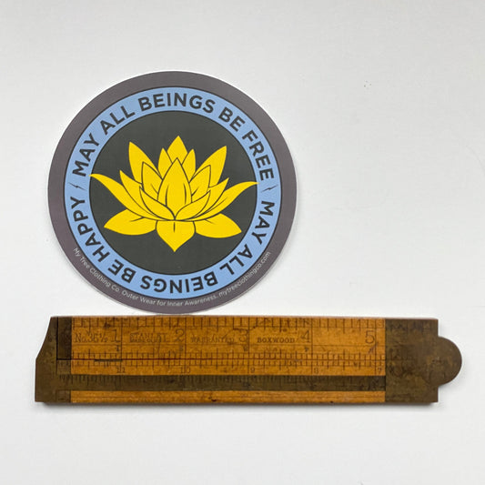 Circular sticker with yellow lotus flower design and text on a white background, accompanied by a wooden ruler for scale.