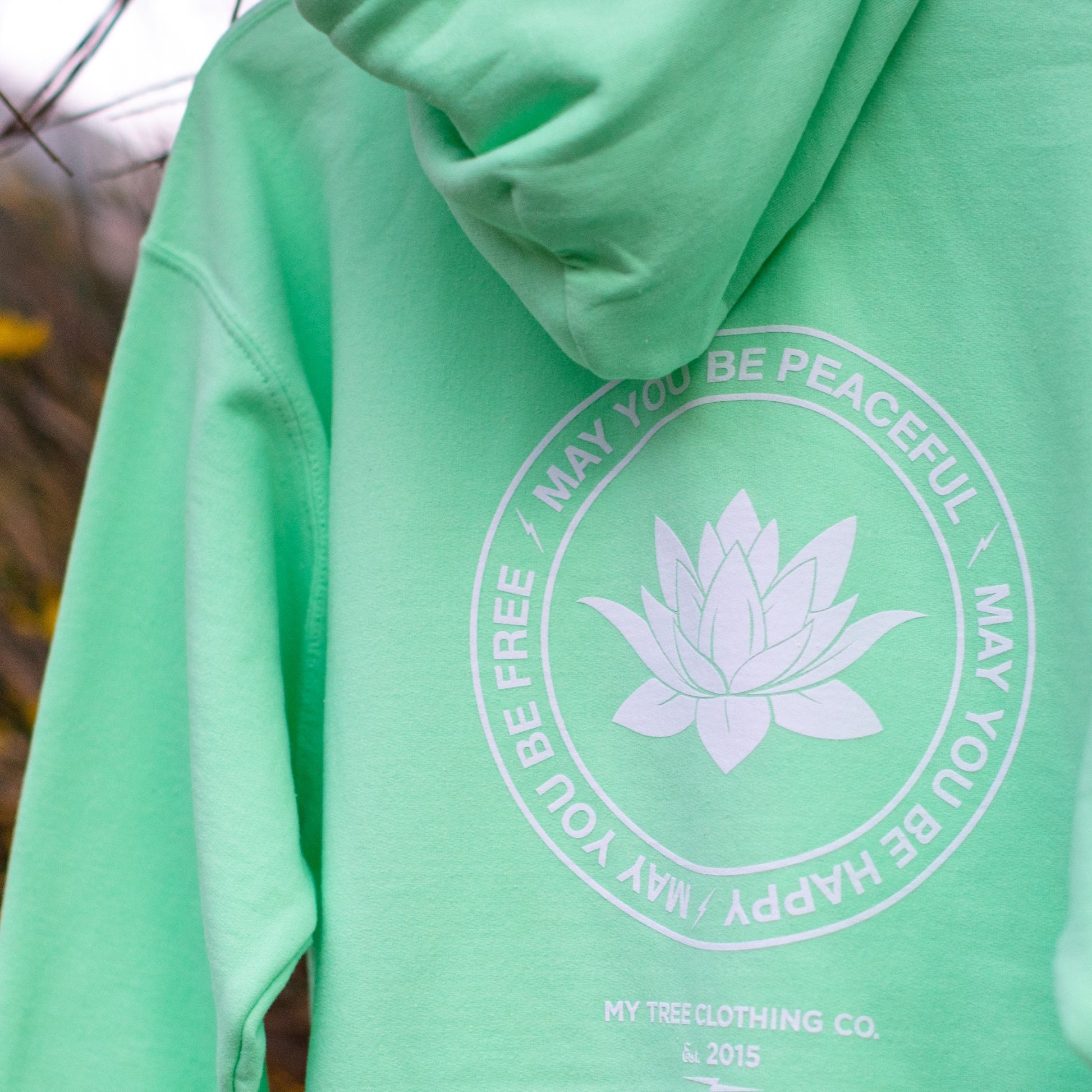 Green hoodie with a white lotus flower design and text on the back, brand 'My Tree Clothing Co.' visible.