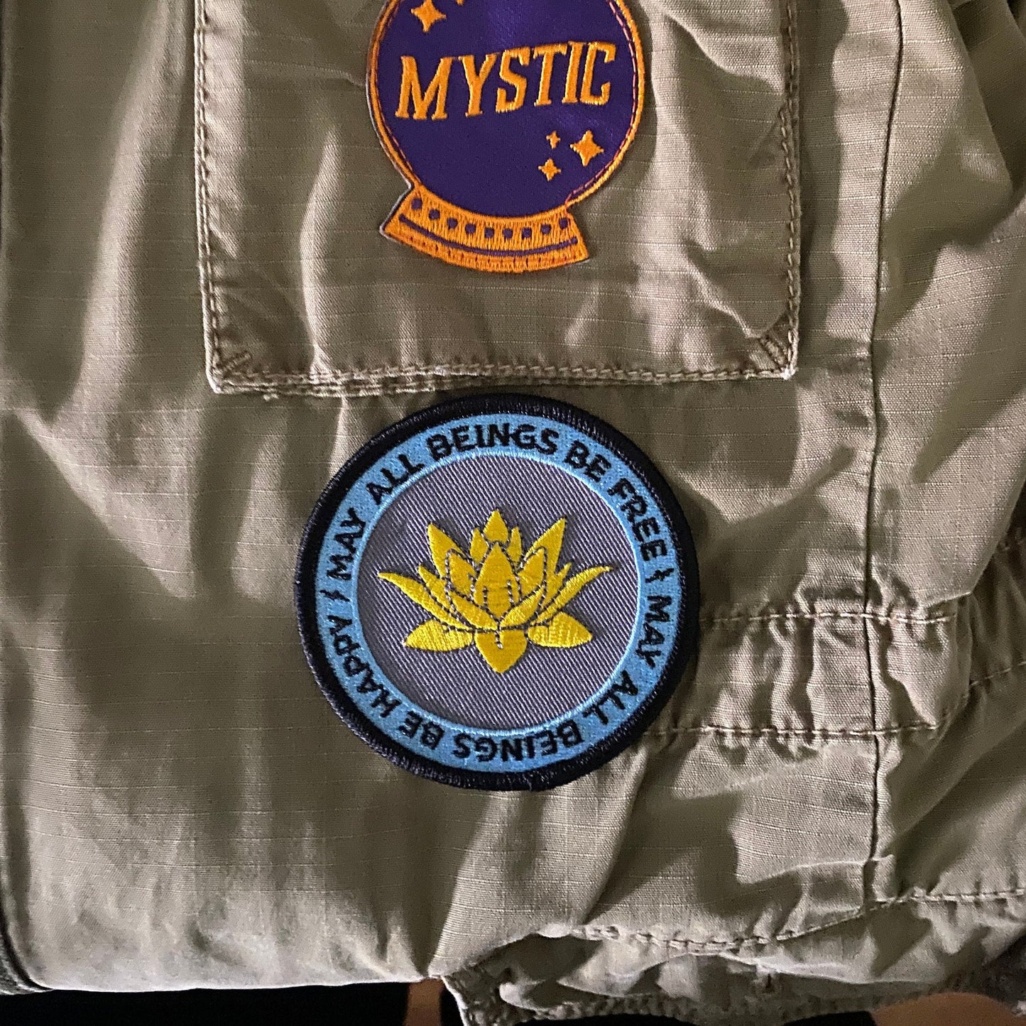 Two patches on a beige jacket: one with 'Mystic' text and a purple patch, the other with a yellow lotus flower and blue text.