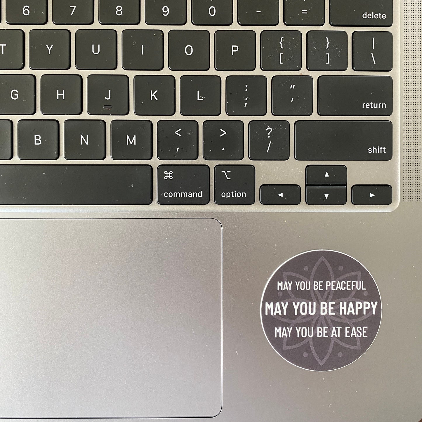 Laptop keyboard with a 2" circular sticker with text, may you be peaceful may you be happy may you be at ease, on the palm rest area