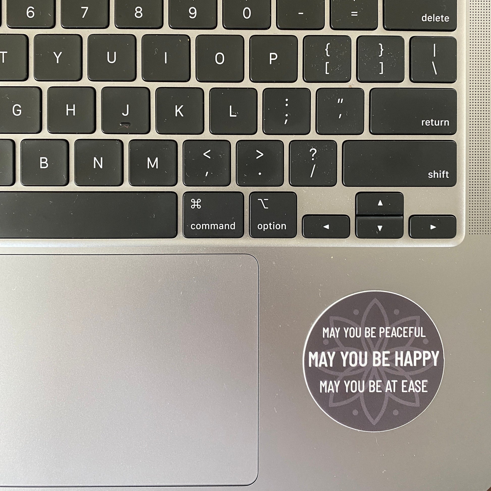 Laptop keyboard with a 2" circular sticker with text, may you be peaceful may you be happy may you be at ease, on the palm rest area
