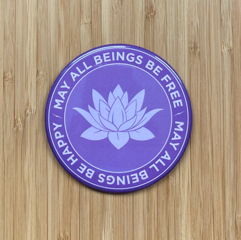 Purple magnet with lotus design and text, may all beings be free may all beings be happy, with lotus flower design and text on a wooden surface.