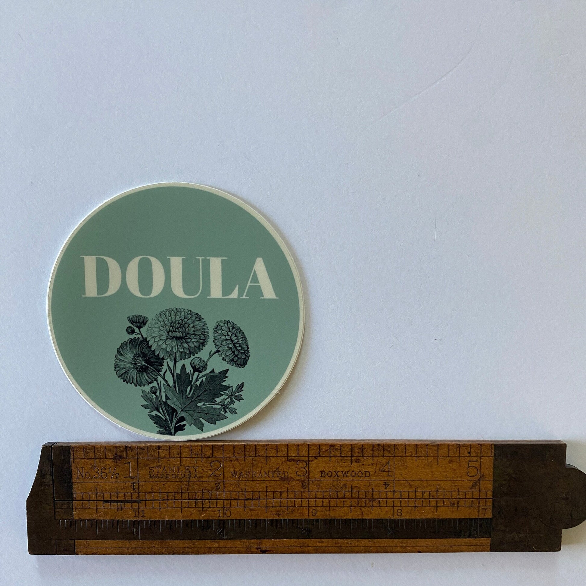 Green coaster with 'DOULA' text and floral design on a white surface with a ruler for scale.