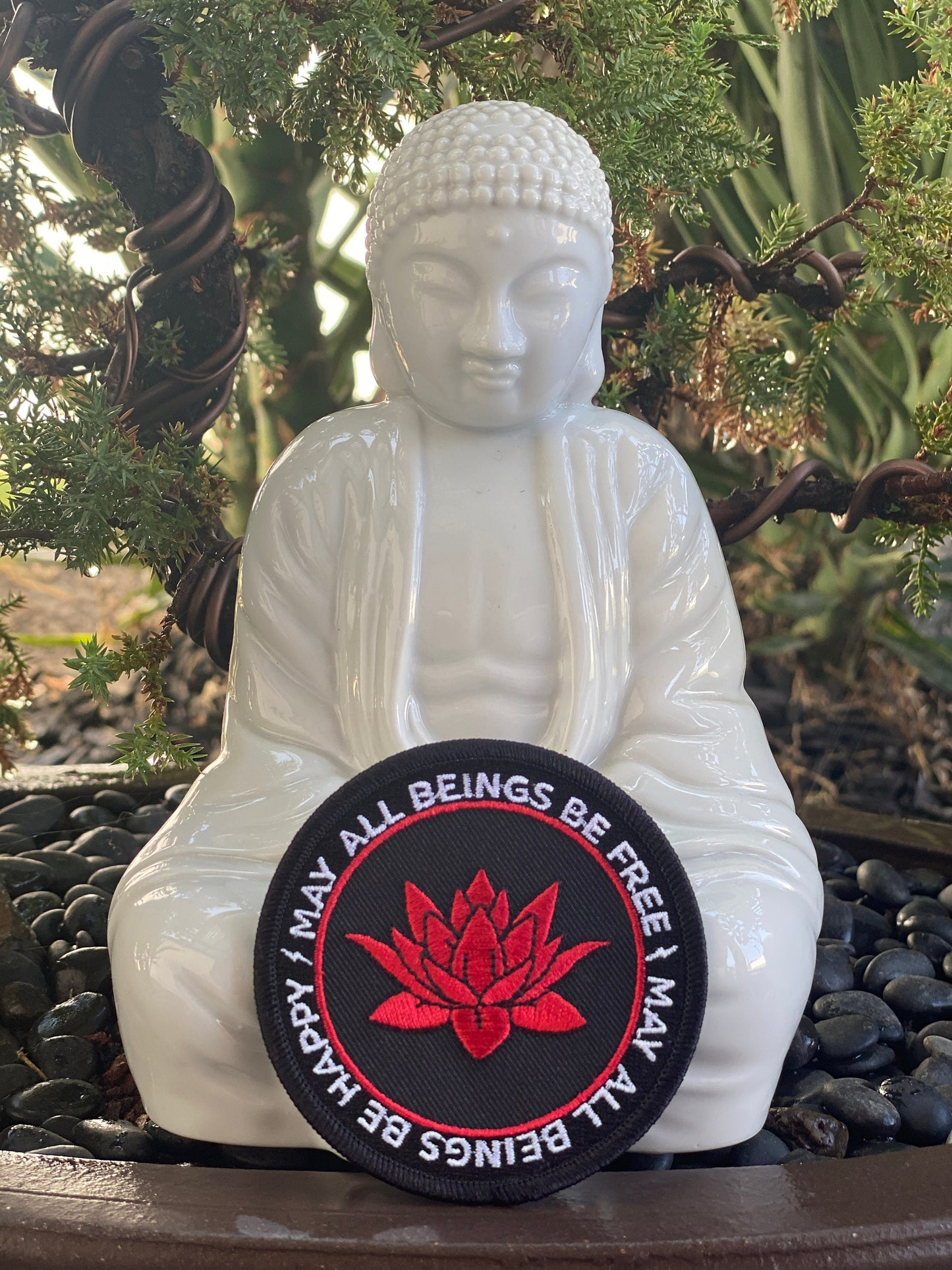 White Buddha statue with a 3" round patch with a red lotus flower and the text, may all beings be free may all beings be happy.