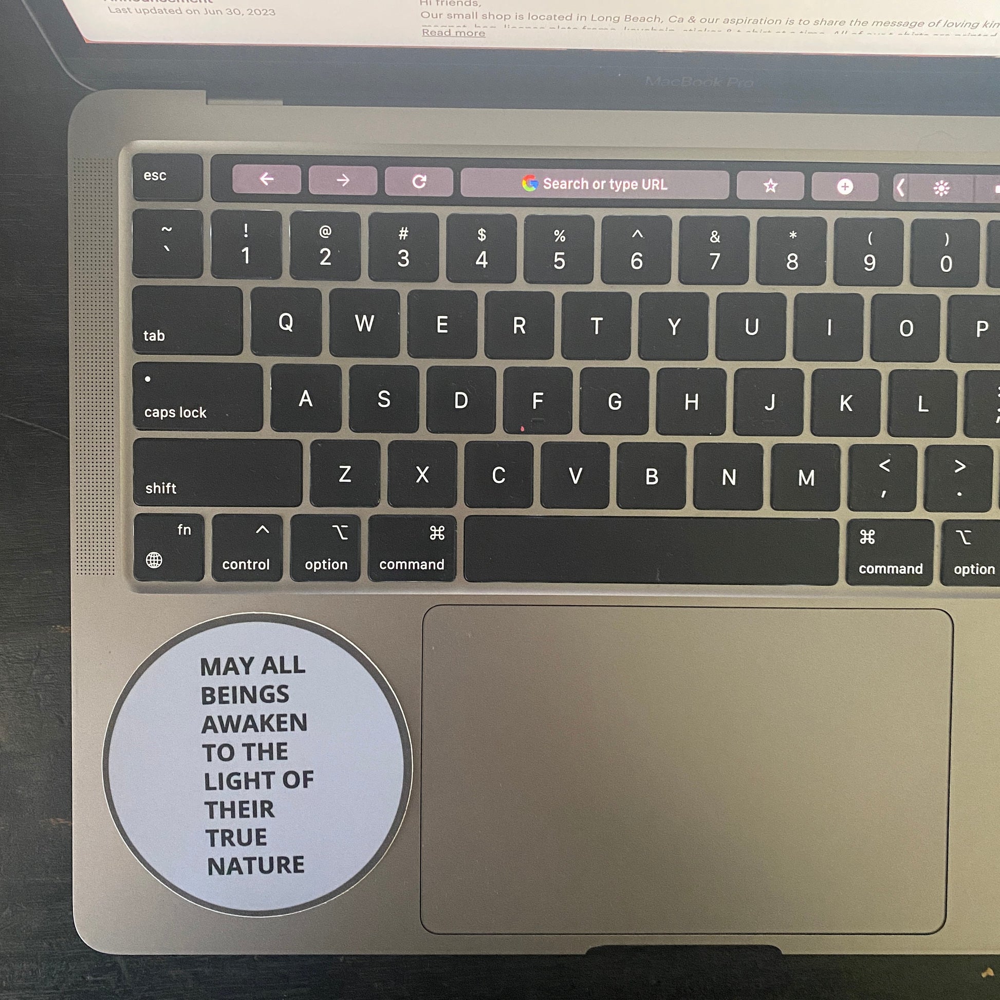 Laptop keyboard with a circular sticker with the text, may all beings awaken to the light of their true nature, on a dark surface. 