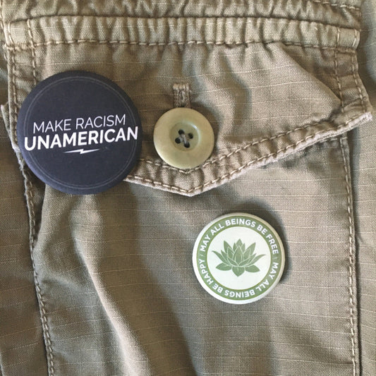 Button on a jacket with 'Make Racism Unamerican' and one light green 1.25" circular Buddhist pin back button with text and a lotus symbol.