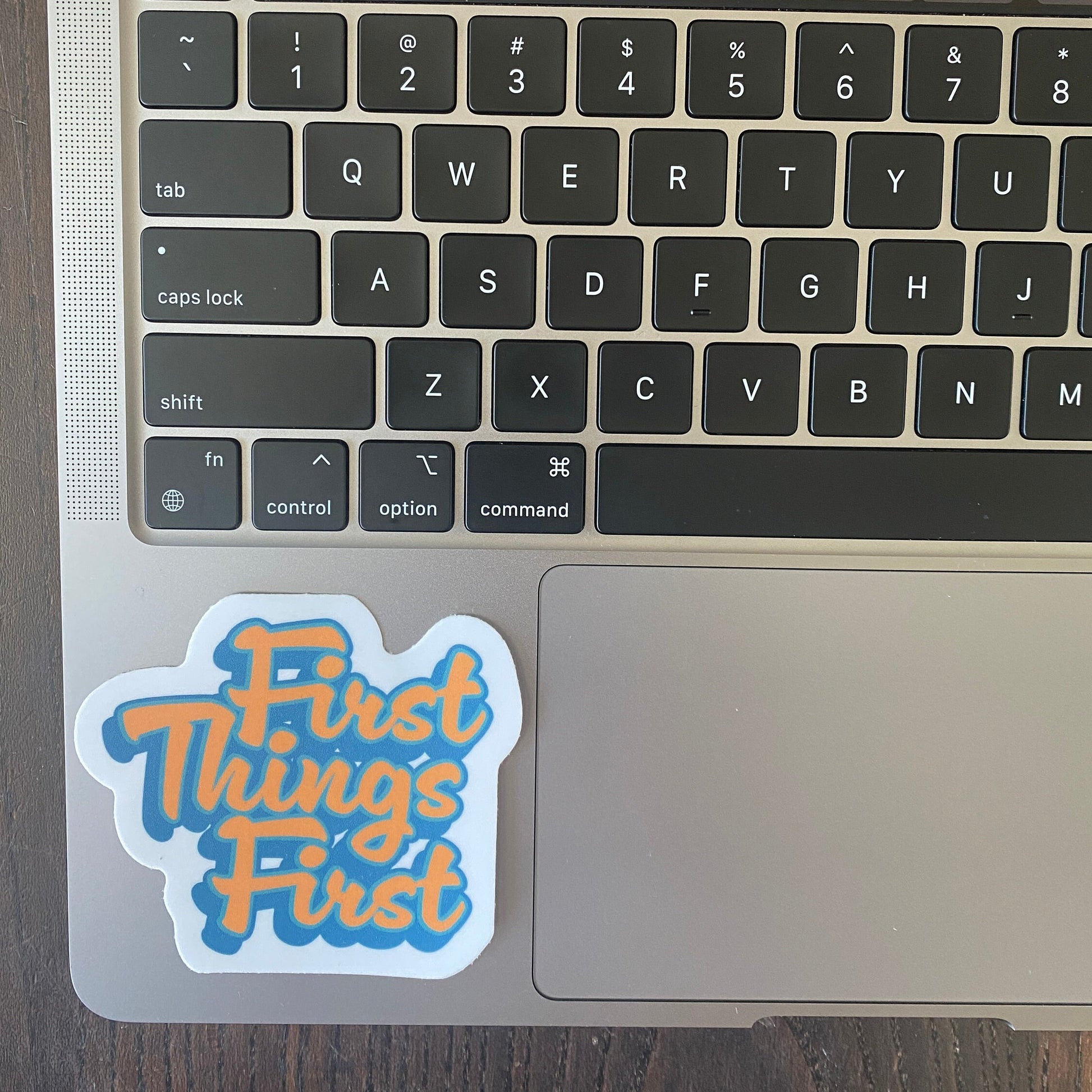 Laptop keyboard with a 'First Things First' sticker on the palm rest area.