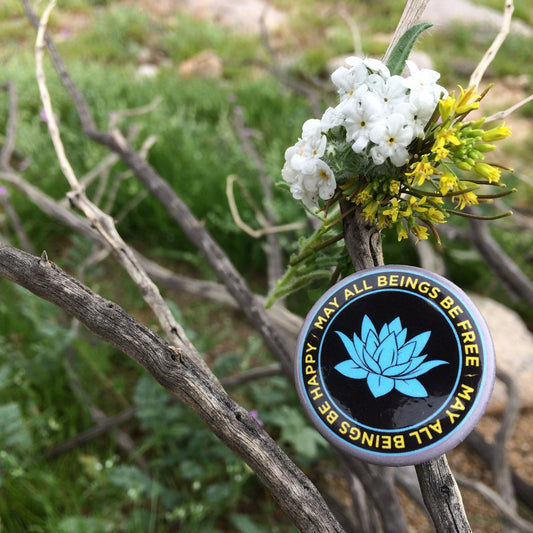 1.25" black and blue lotus button with the Buddhist prayer, may all beings be free may all beings be happy, on a branch with flowers.
