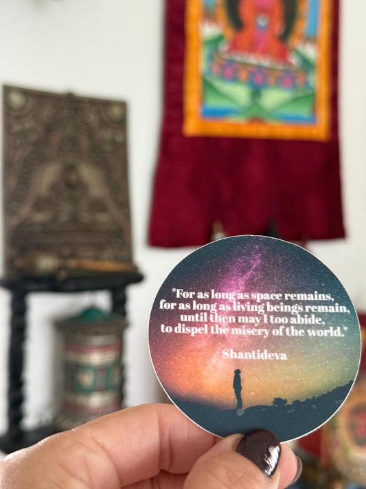 Sticker with Shantideva quote held in front of a blurred background with religious art.