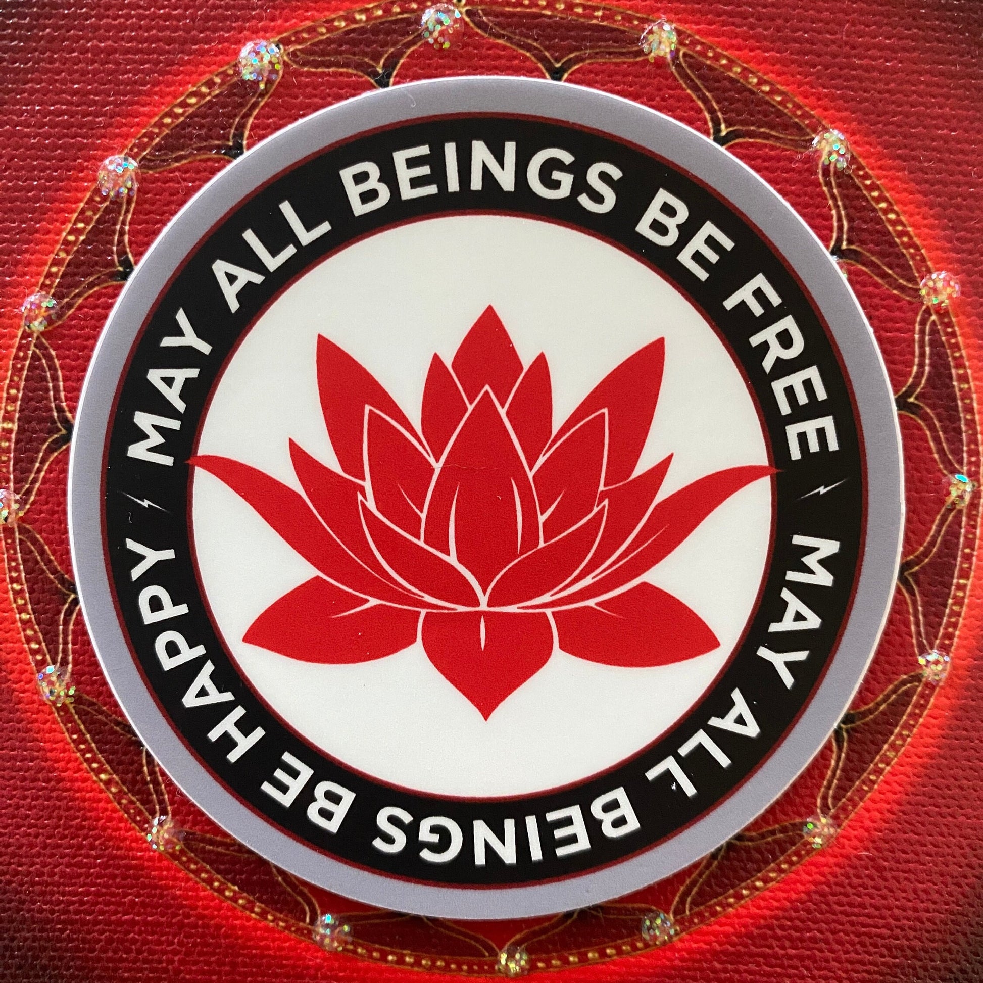 Circular emblem with red lotus flower and text 'May all beings be free, happy' on a red background