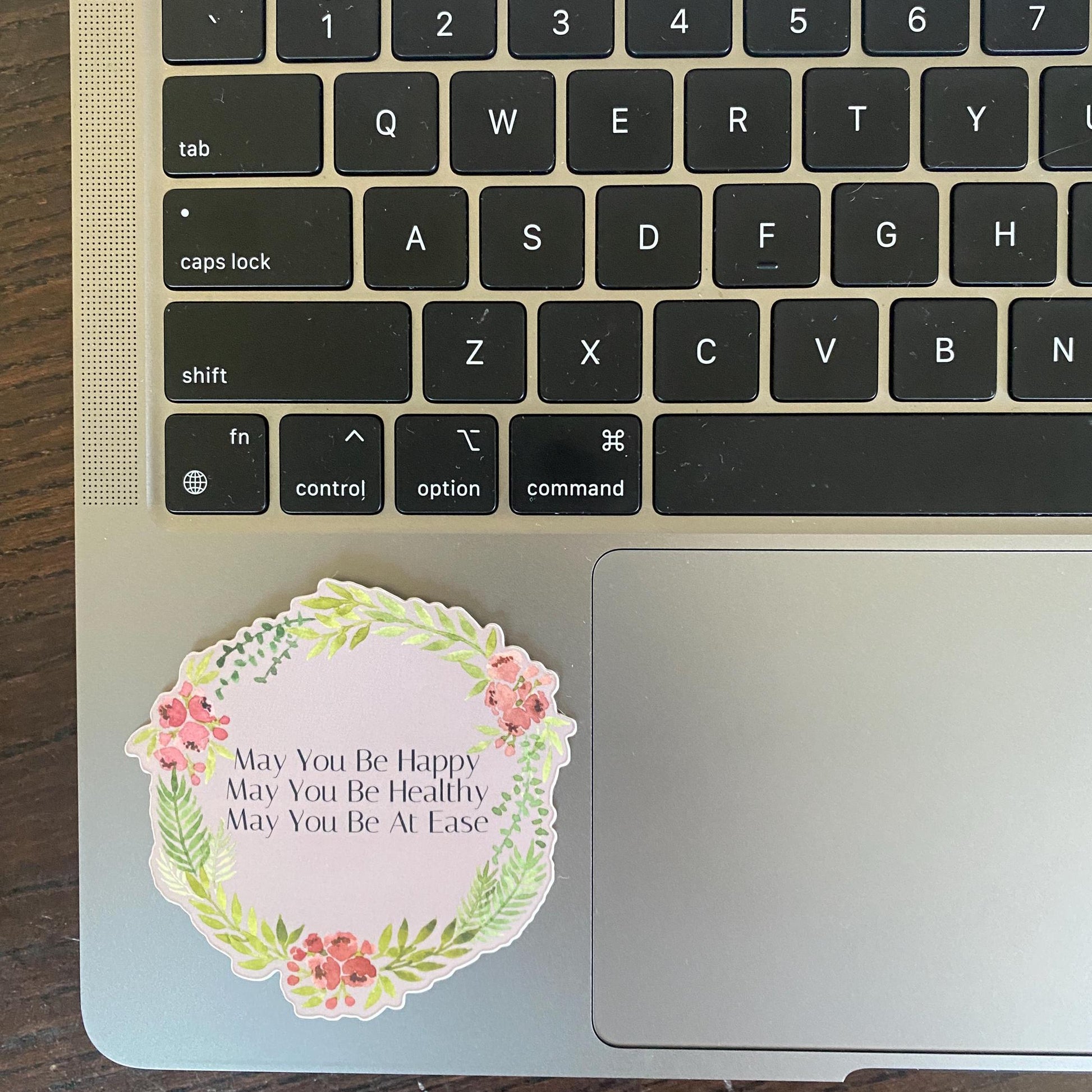 Laptop keyboard with a decorative sticker that reads, may you be happy, may you be healthy, may you be at ease on the palm rest area