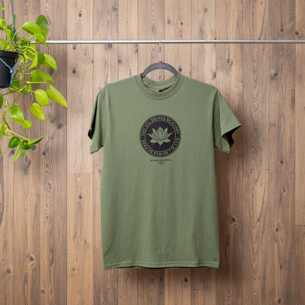 Green Buddhist lotus shirt with the text, May All Beings Be Happy May All Beings Be Free, on a hanger against a wooden background.