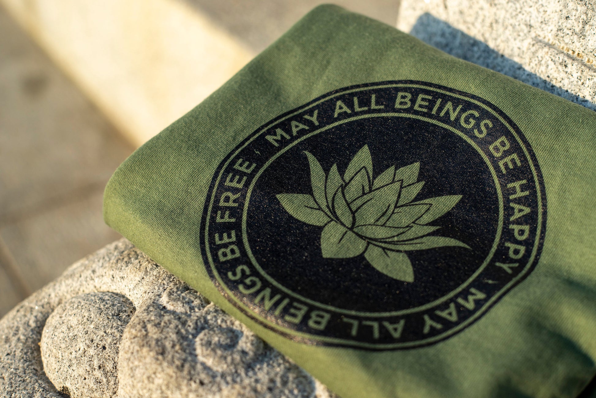 Close up photo of green Buddhist lotus shirt with the text, May All Beings Be Happy May All Beings Be Free.