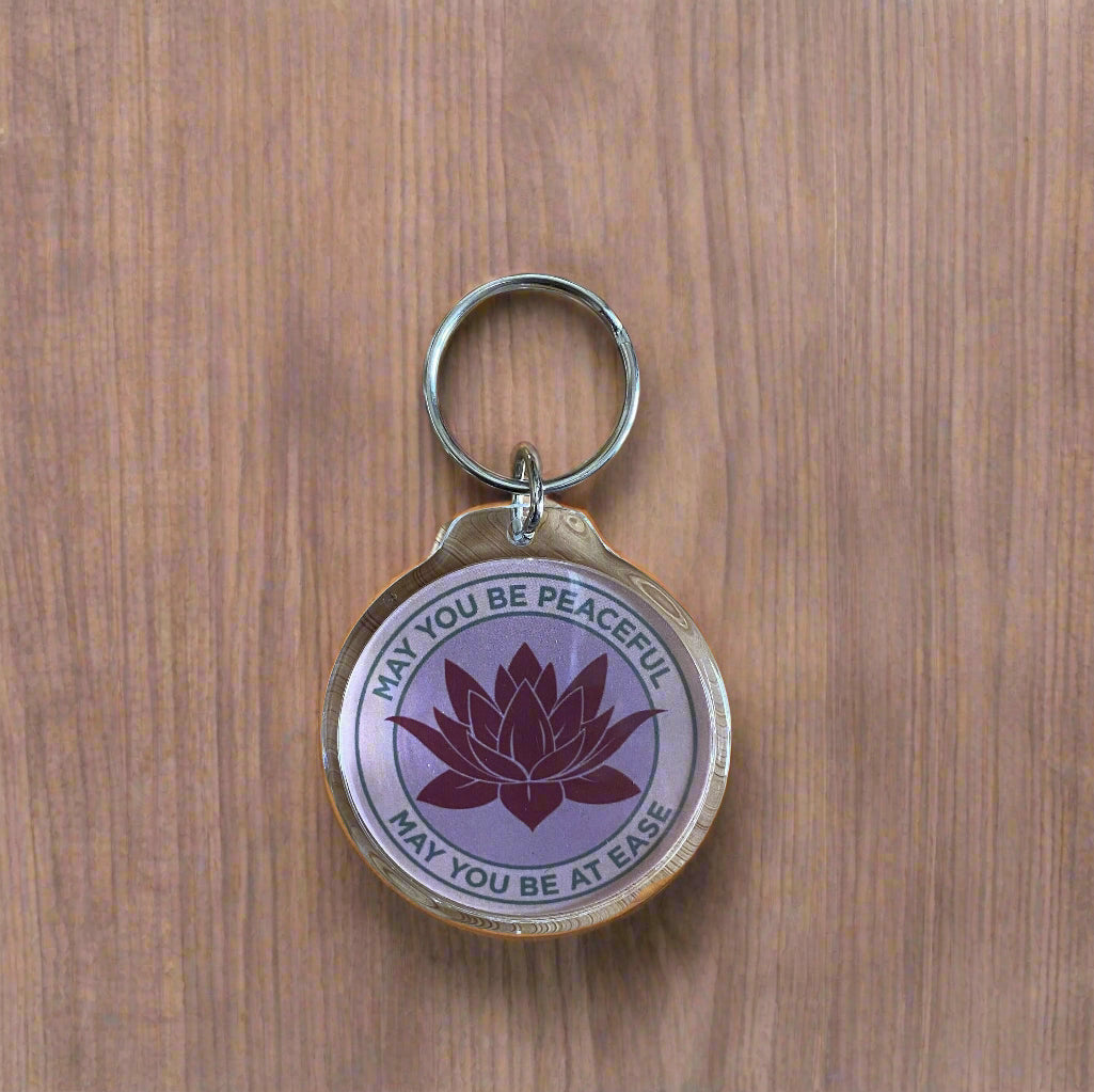Keychain with lotus flower design and text, may you be peaceful may you be at ease, on a wooden surface