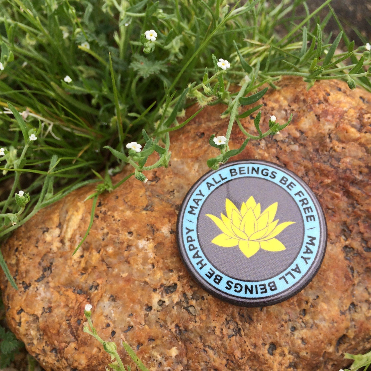 Round badge with a yellow lotus flower design on a rock surrounded by greenery